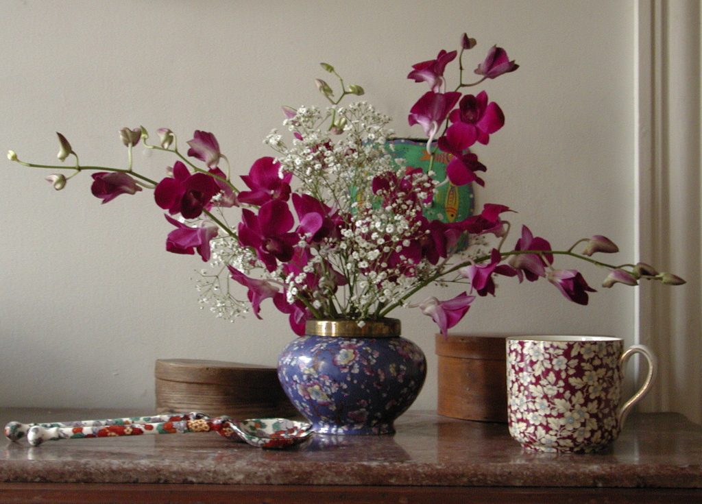 Magenta orchids in a blue and white porcelain vase beside a chintz mug on a stone shelf