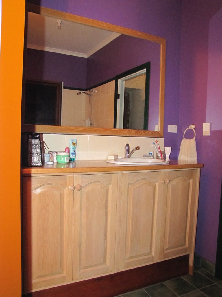 A bathroom vanity with pale wood cabinets and a large mirror against a violet wall