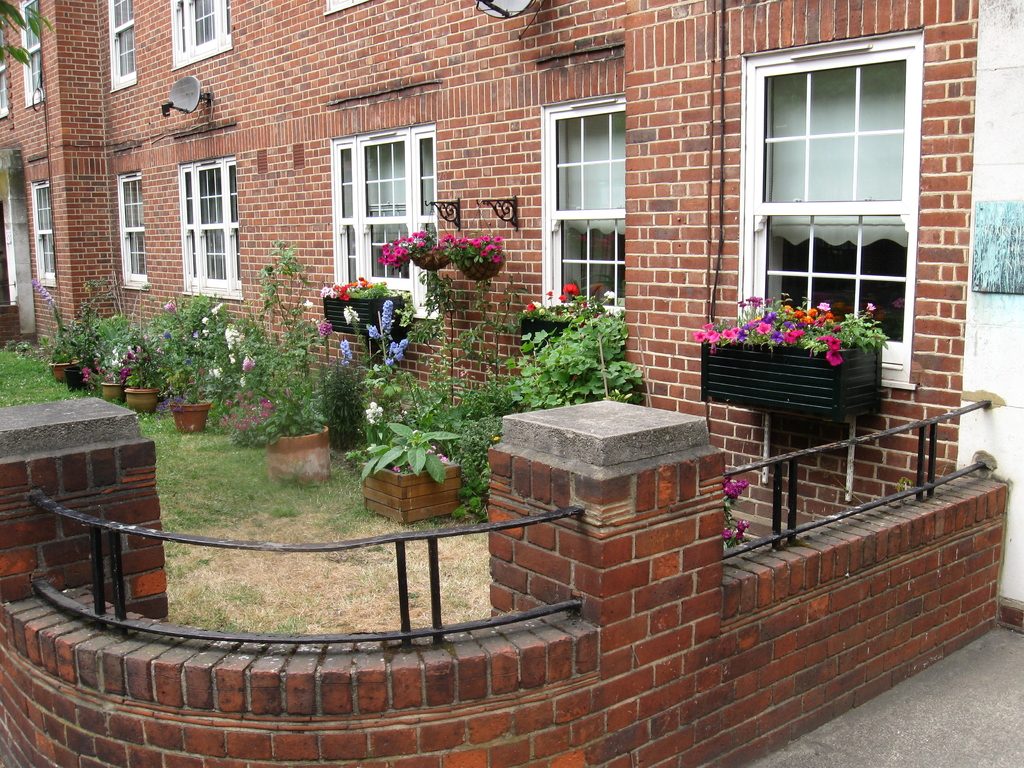 Brick house windows with flower boxes above a small courtyard garden